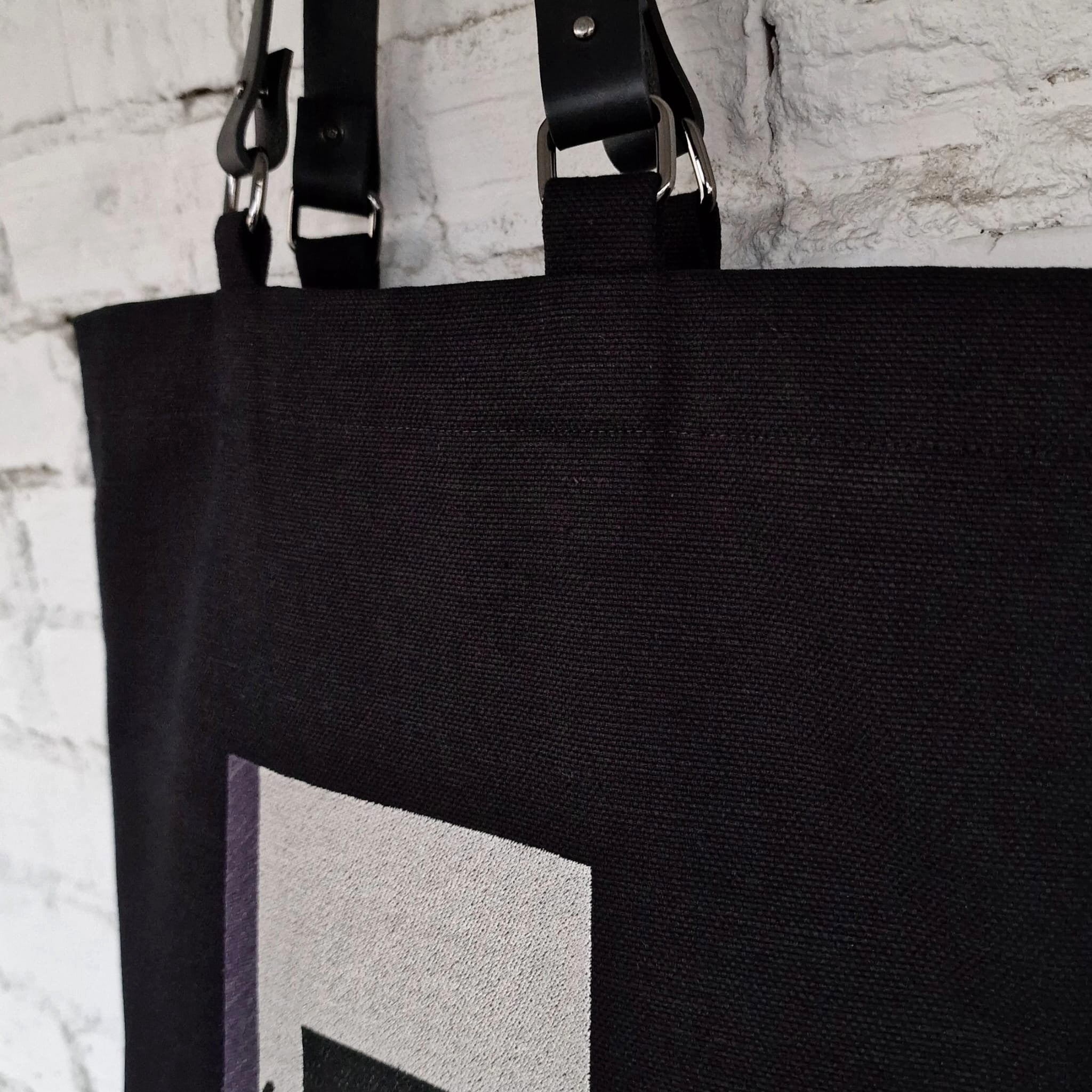 Close-up of black tote bag top corner showing faux leather handles with metal hardware"