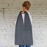 Back side of a grey linen hobo bag held on shoulder, featuring clean stitching and discreet designer label