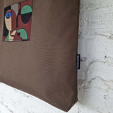 Close-up of abstract embroidered face design and RIMALINUM fabric label on dark brown cotton tote bag