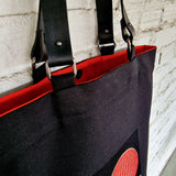 Black tote bag with red accents against a light gray brick wall.