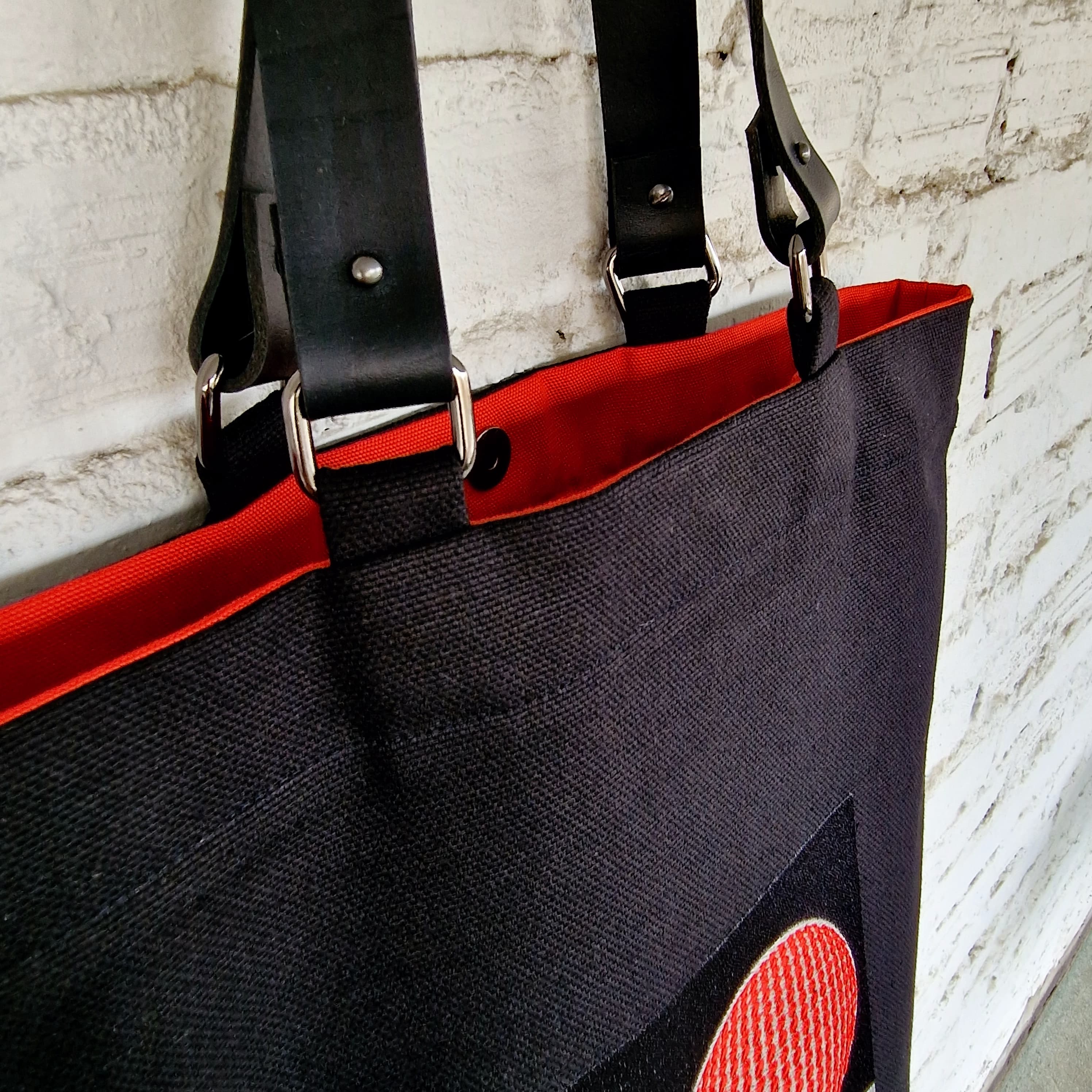 Black tote bag with red accents against a light gray brick wall.