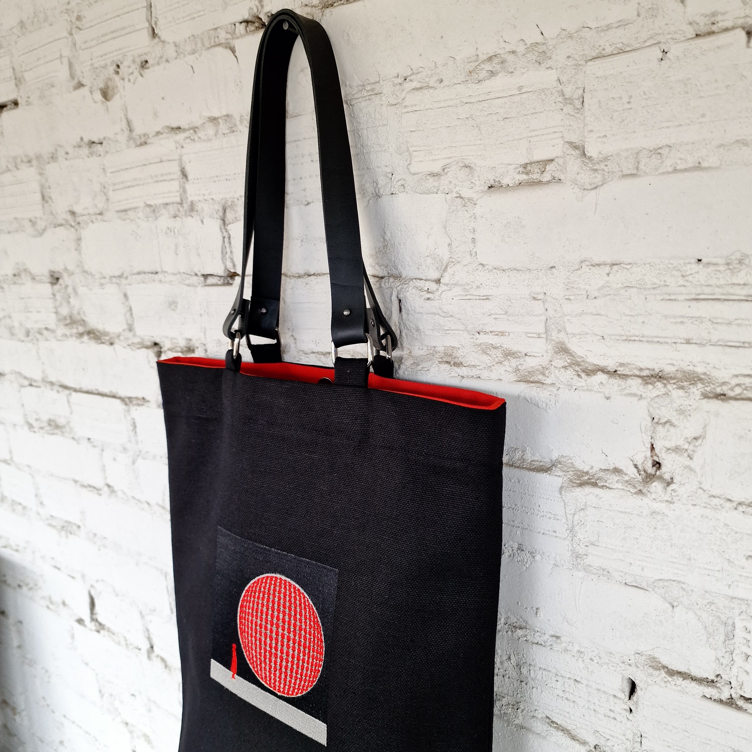 Close-up of black leather handles with metal hardware and vibrant red lining at the top of the tote bag
