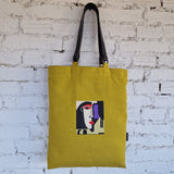 Close-up of mustard yellow linen tote bag with black leather straps and purple cotton lining, showing metal ring attachments and stitching details