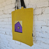 Close-up of embroidered geometric house motif on yellow canvas tote bag, with visible Rimalinum brand tag on side seam
