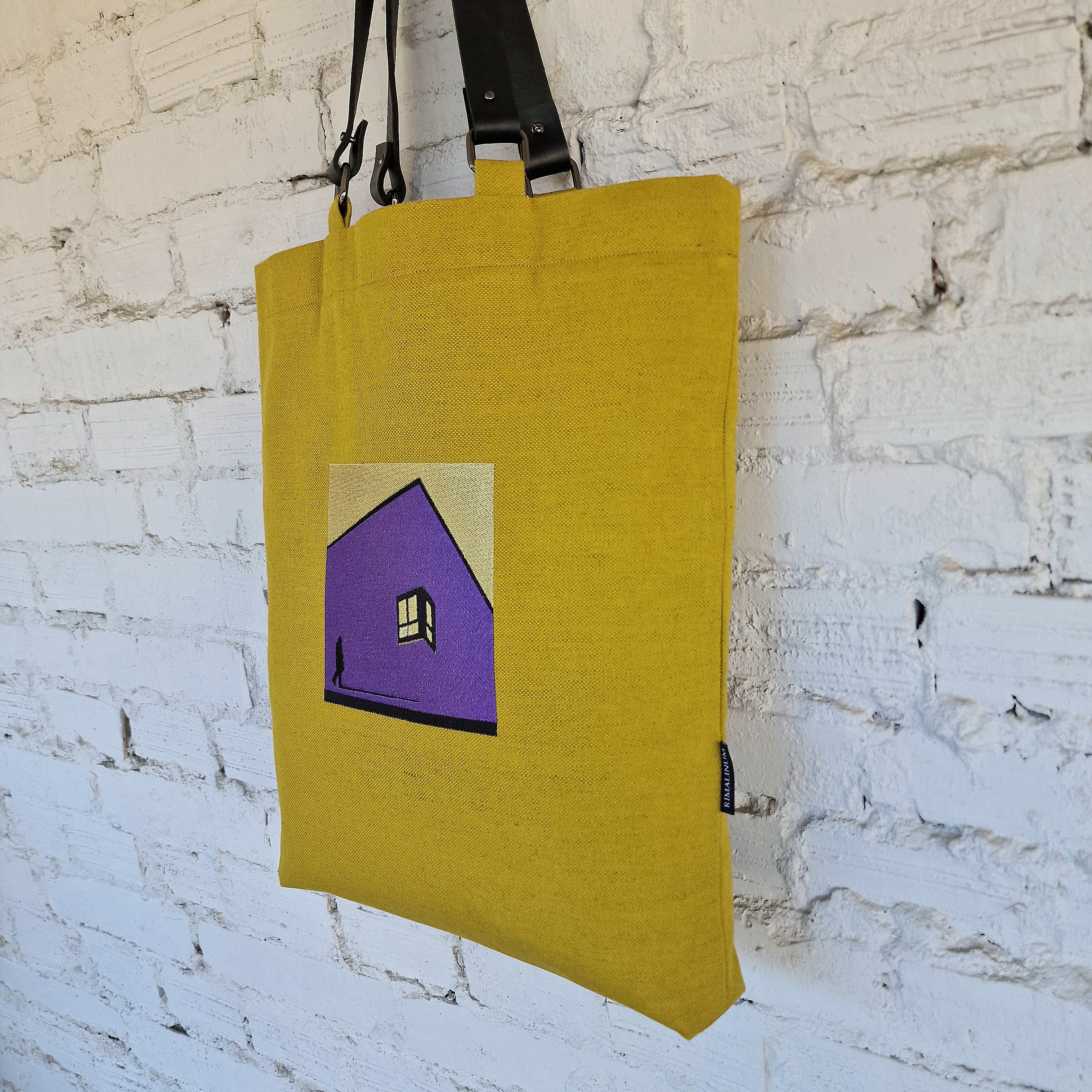 Close-up of embroidered geometric house motif on yellow canvas tote bag, with visible Rimalinum brand tag on side seam