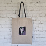 Full front view of large natural linen tote bag with black detachable shoulder straps and unique modern embroidery.