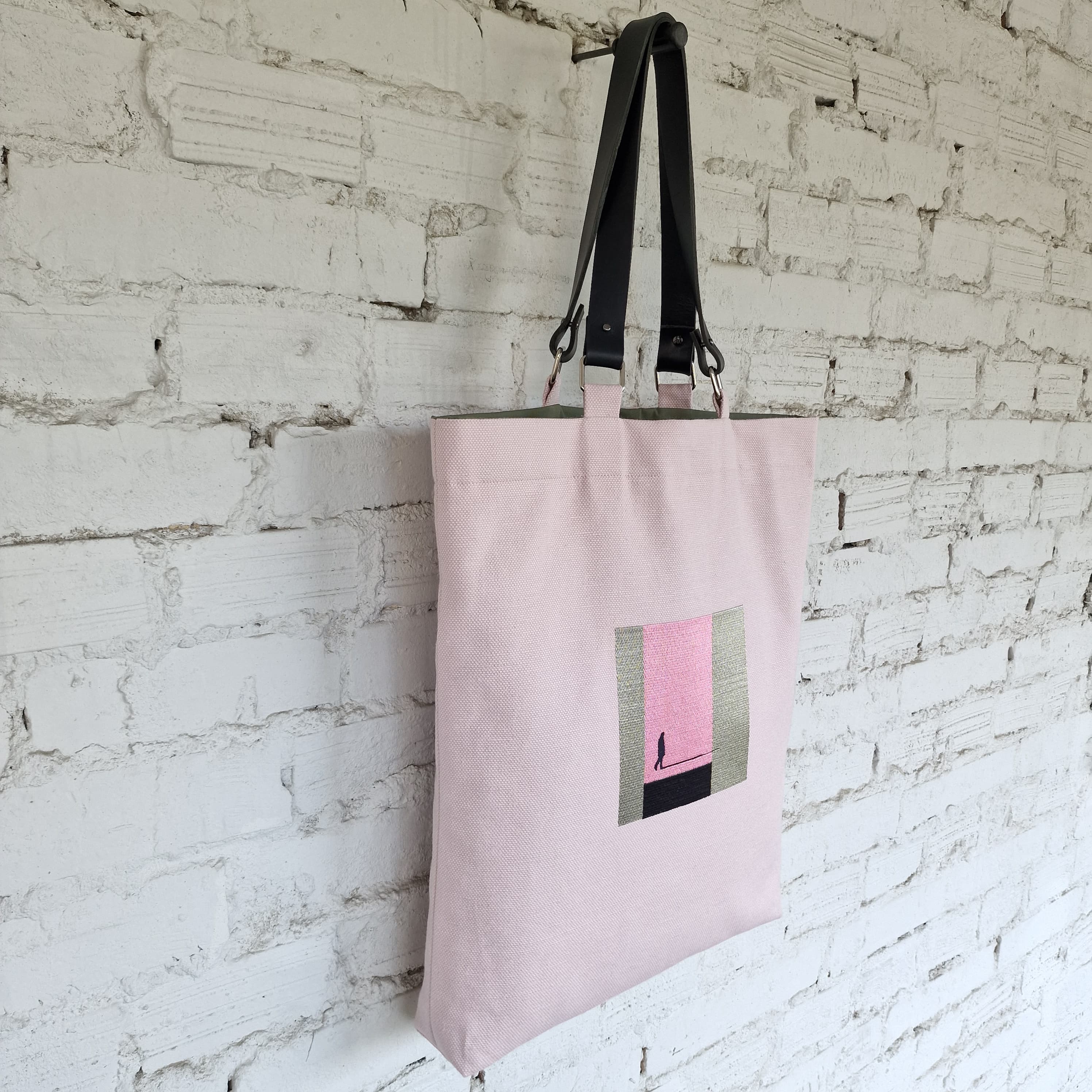 Pink tote bag with a geometric design hanging against a white brick wall.