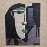 Detailed close-up of embroidered abstract face in green, black, and lilac thread on natural linen – artistic minimalist embroidery