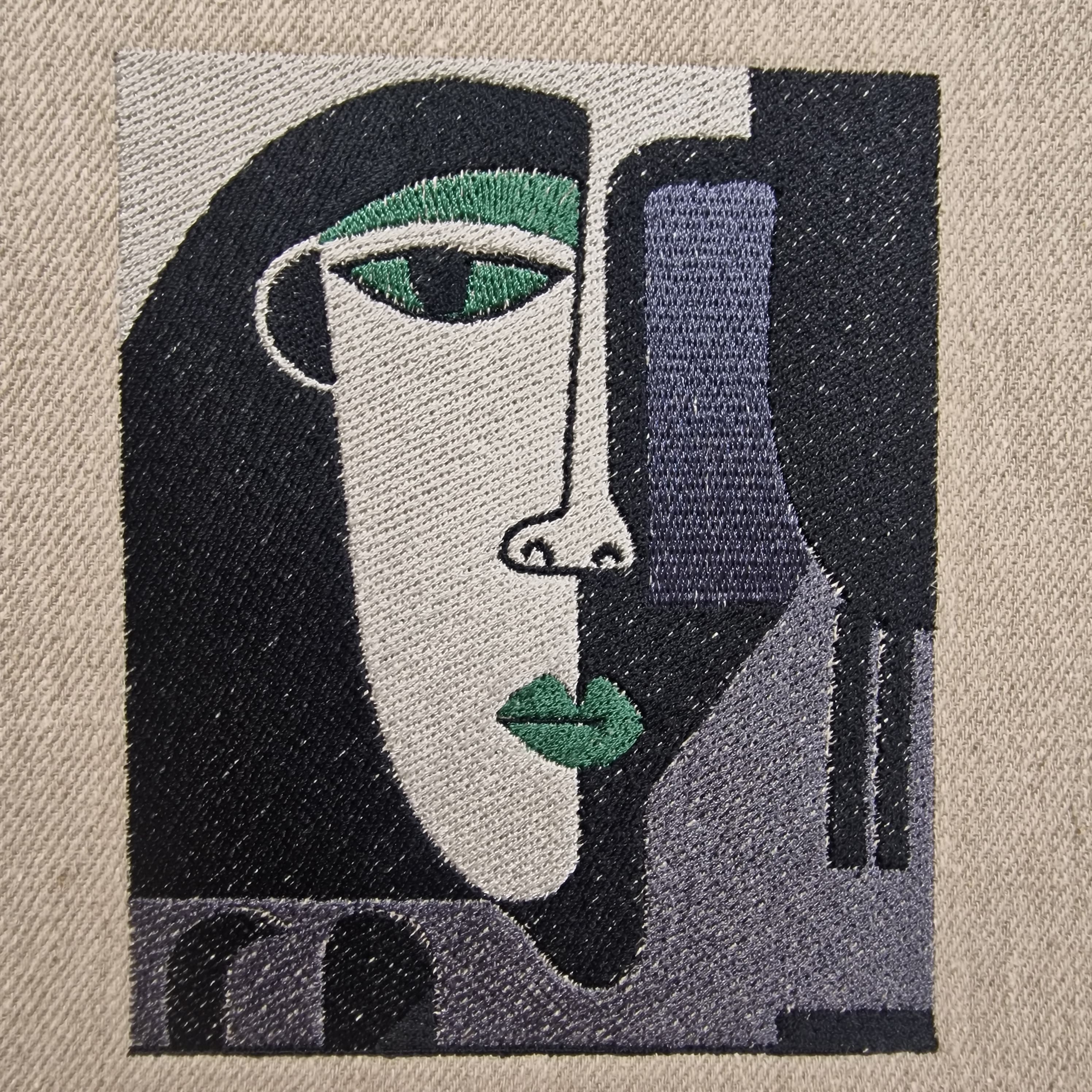 Detailed close-up of embroidered abstract face in green, black, and lilac thread on natural linen – artistic minimalist embroidery