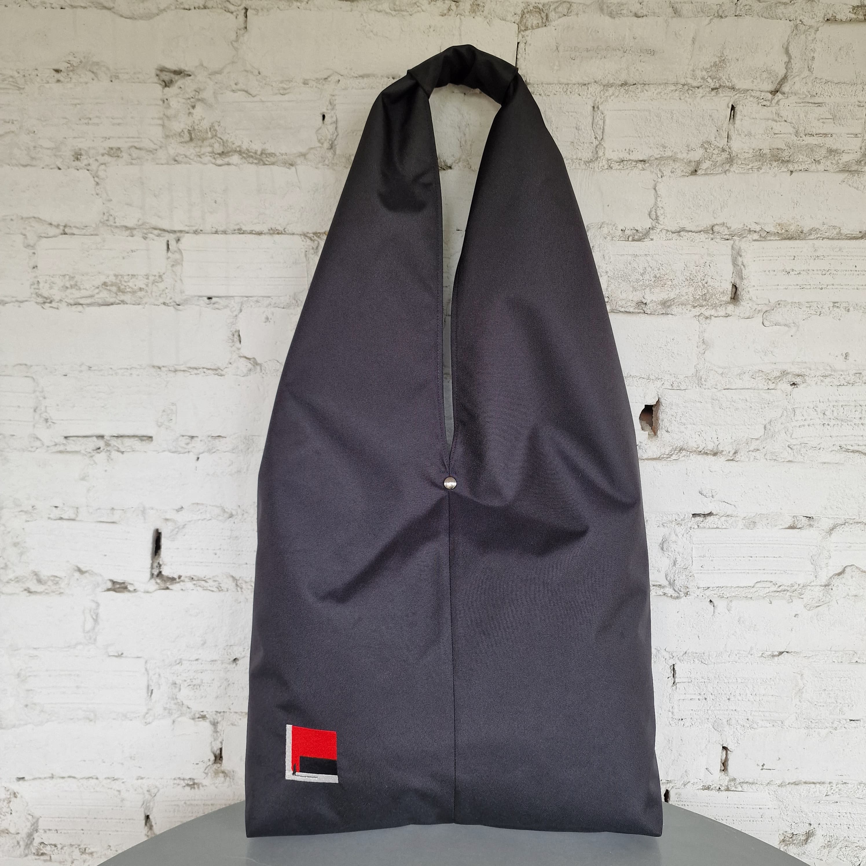 Front view of black HOBO bag with minimalist embroidered design, hanging on white wall
