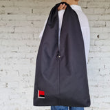 Model holding oversized minimalist black shoulder bag in urban environment