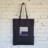 Full front view of black tote bag with grey and purple embroidery on a bright background