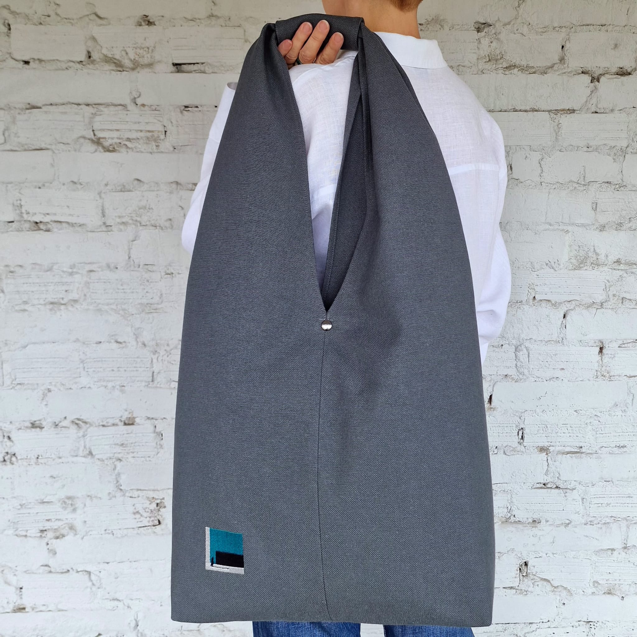 Handmade dark grey shoulder tote with deep V shape and soft drape, worn on the back by short-haired woman
