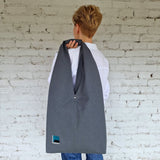 Woman wearing a large dark grey linen hobo bag on shoulder, minimalistic urban style tote with abstract embroidery