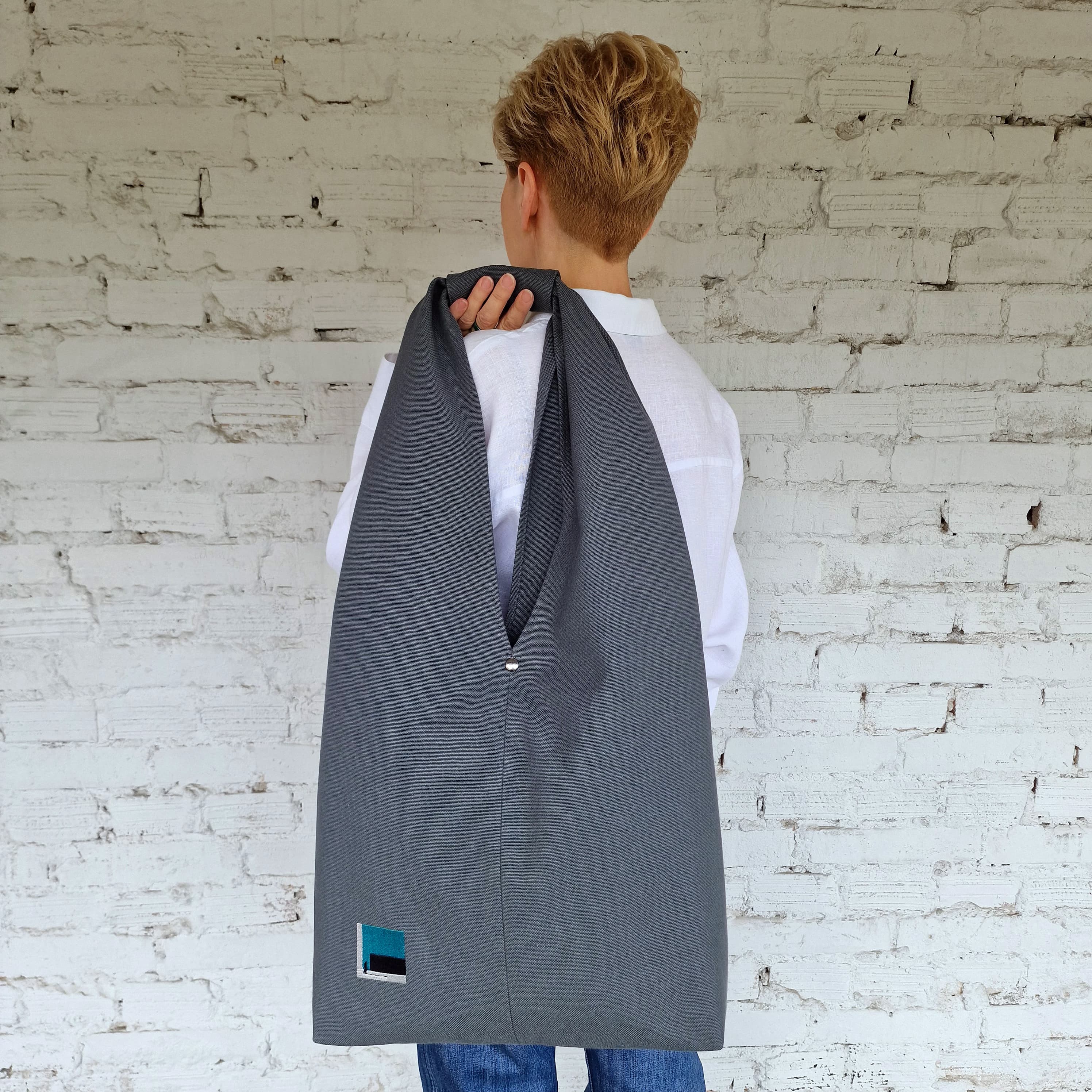 Woman wearing a large dark grey linen hobo bag on shoulder, minimalistic urban style tote with abstract embroidery