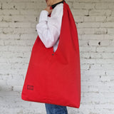 Red reusable bag held by a person against a white brick wall