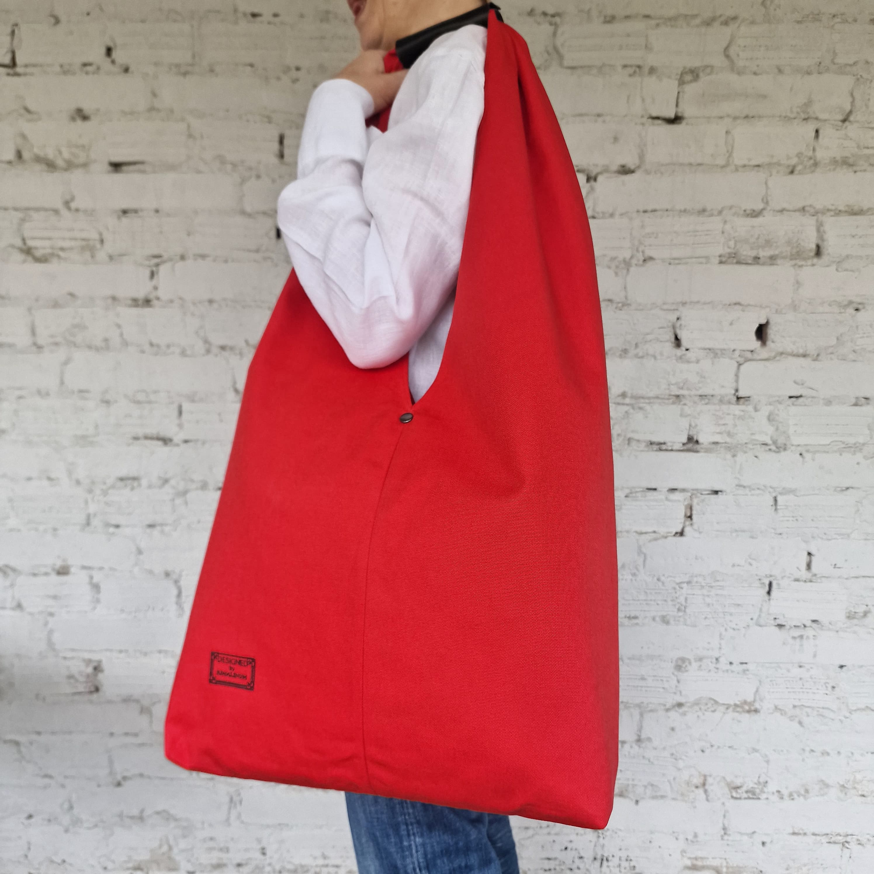 Red reusable bag held by a person against a white brick wall