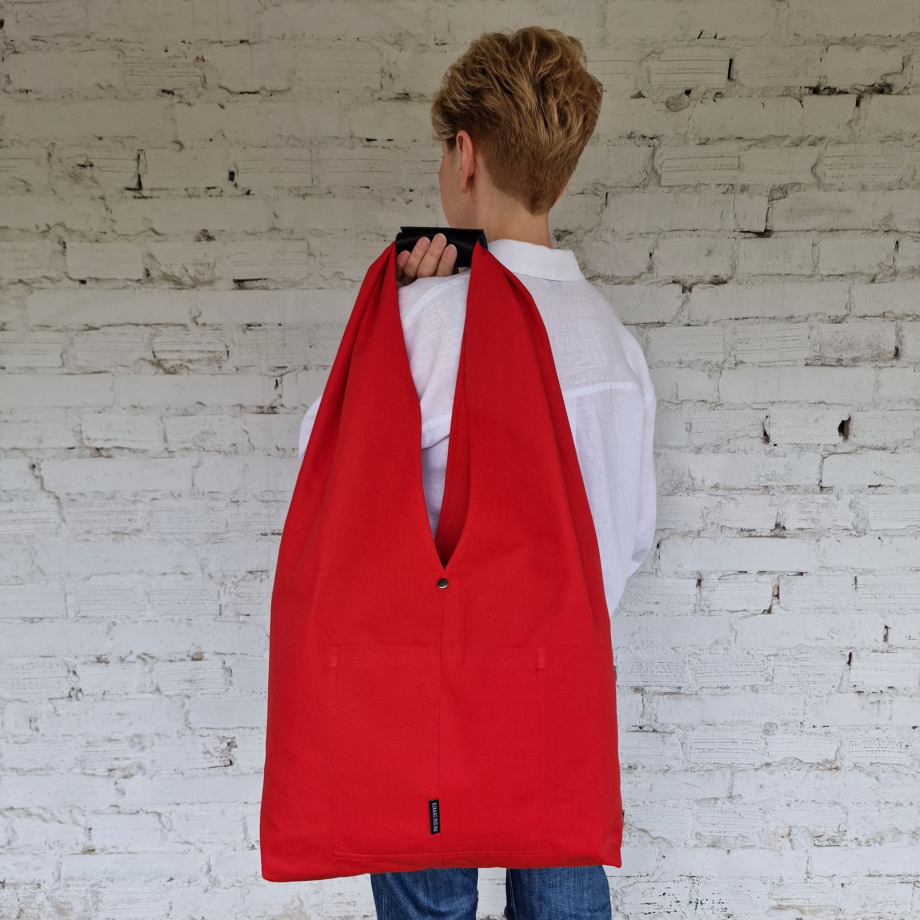 Back view of person holding large foldable red cotton hobo tote bag with leather snap detail