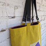 Top view of mustard yellow tote bag showing black leather handles and visible purple lining