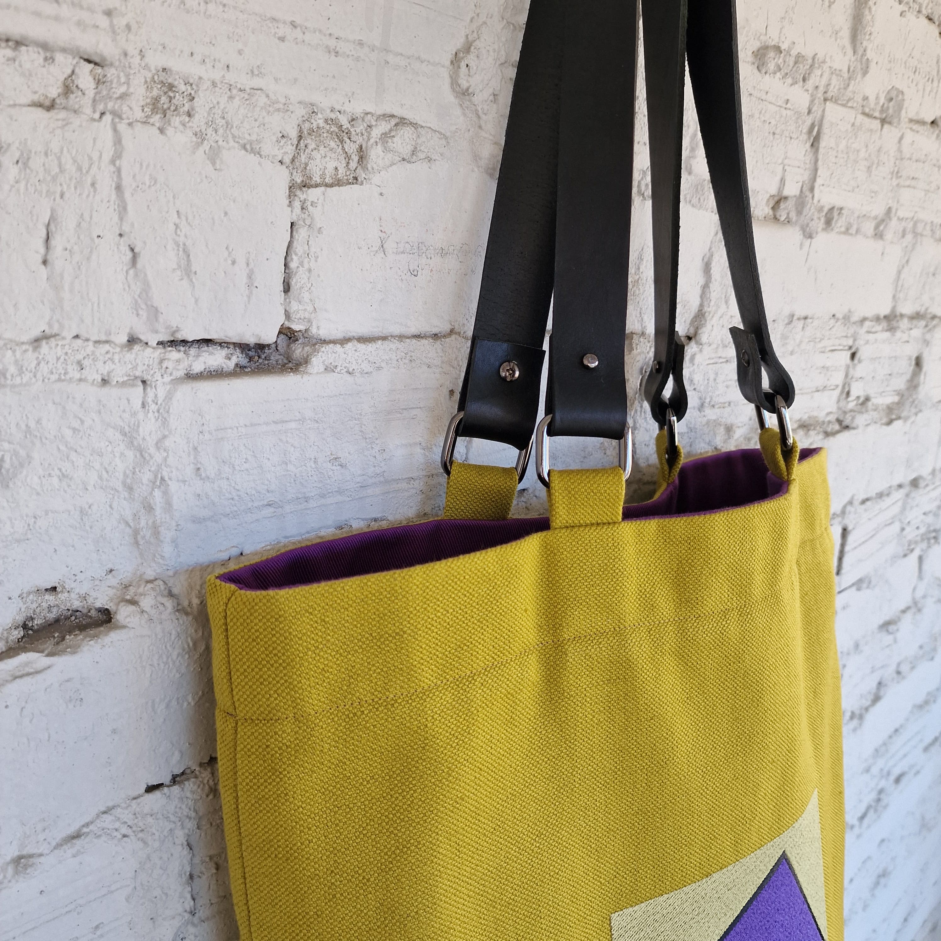 Top view of mustard yellow tote bag showing black leather handles and visible purple lining
