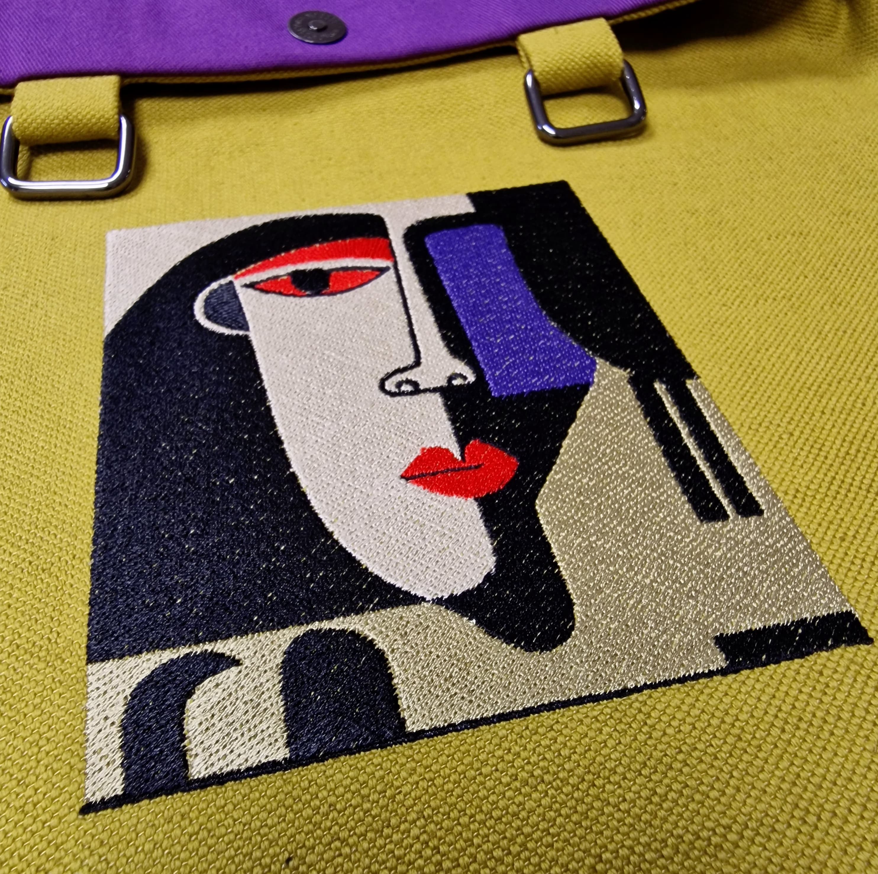 Close-up of embroidered cubist face in red, black, white, and purple thread on yellow linen tote with purple cotton lining