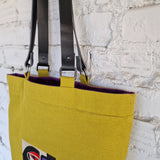 Yellow tote bag with black straps against a stone wall background