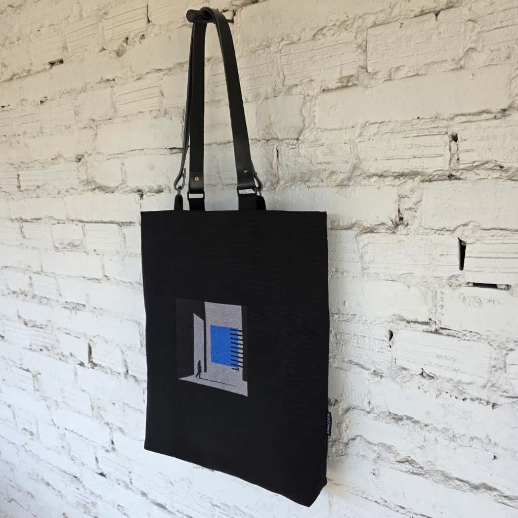 Black tote bag with a graphic design on a white brick wall