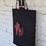 Black tote  bag with red and grey design against a textured white wall