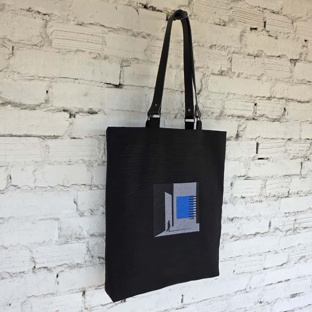 Black linen tote bag with blue geometric embroidery and leather handles