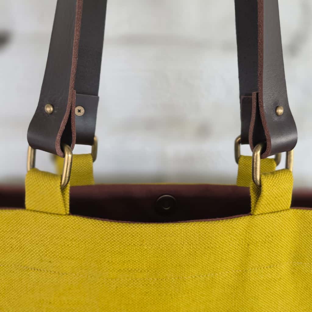 Brown leather handle attachment detail on yellow bag