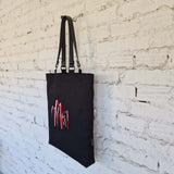 Side view of black linen-cotton tote bag showing Kazys Varnelis “Chairs” embroidery design