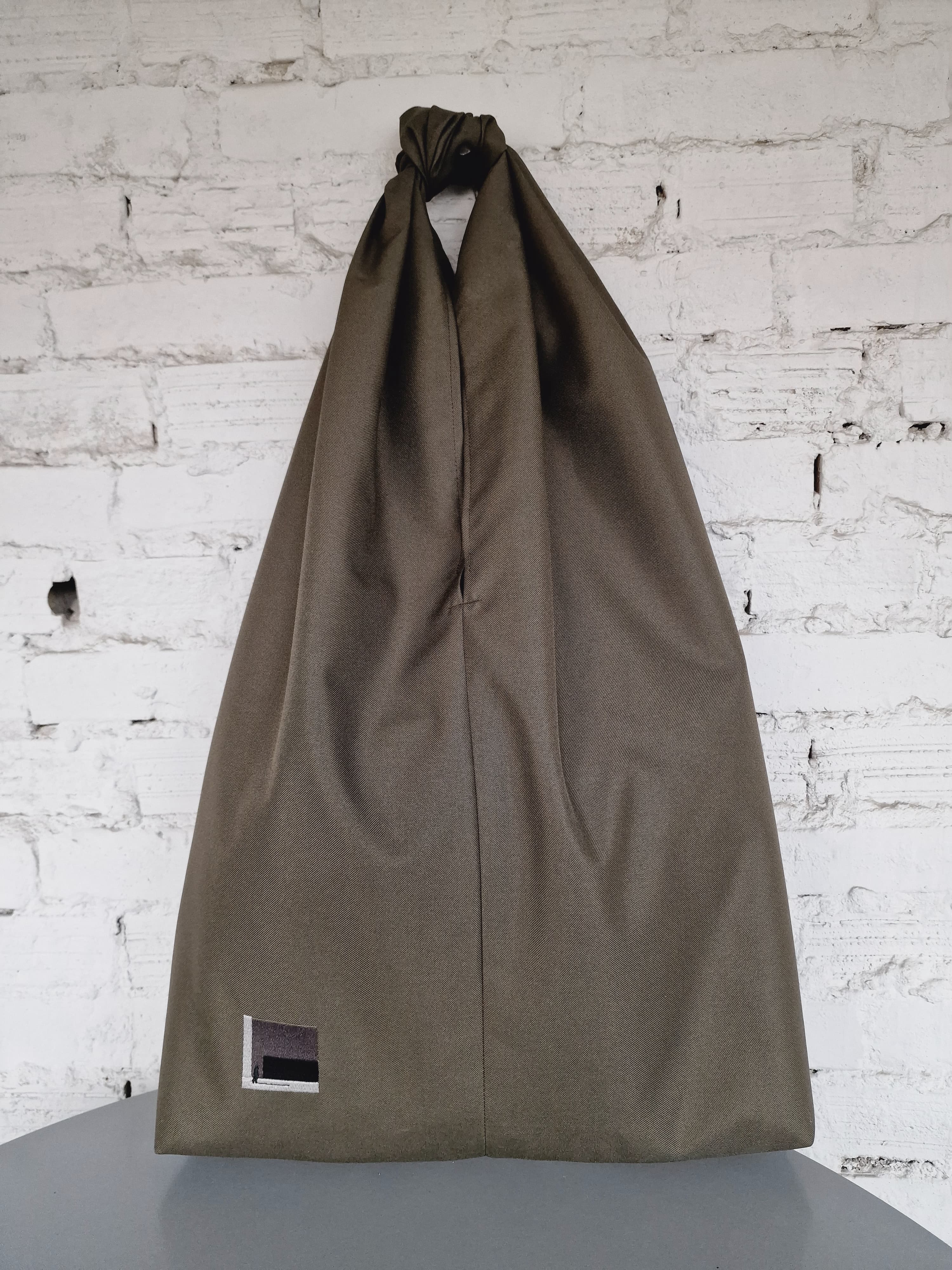 Khaki HOB bag on a gray surface with a white brick wall background 