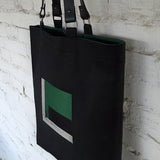 Black linen tote bag photographed from the side to show structure, leather straps, and green fabric interior