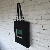 Side view of a black linen tote bag featuring a green geometric embroidered artwork and green interior lining