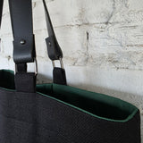 Removable leather strap attachment with metal rings on a black linen tote bag with green lining
