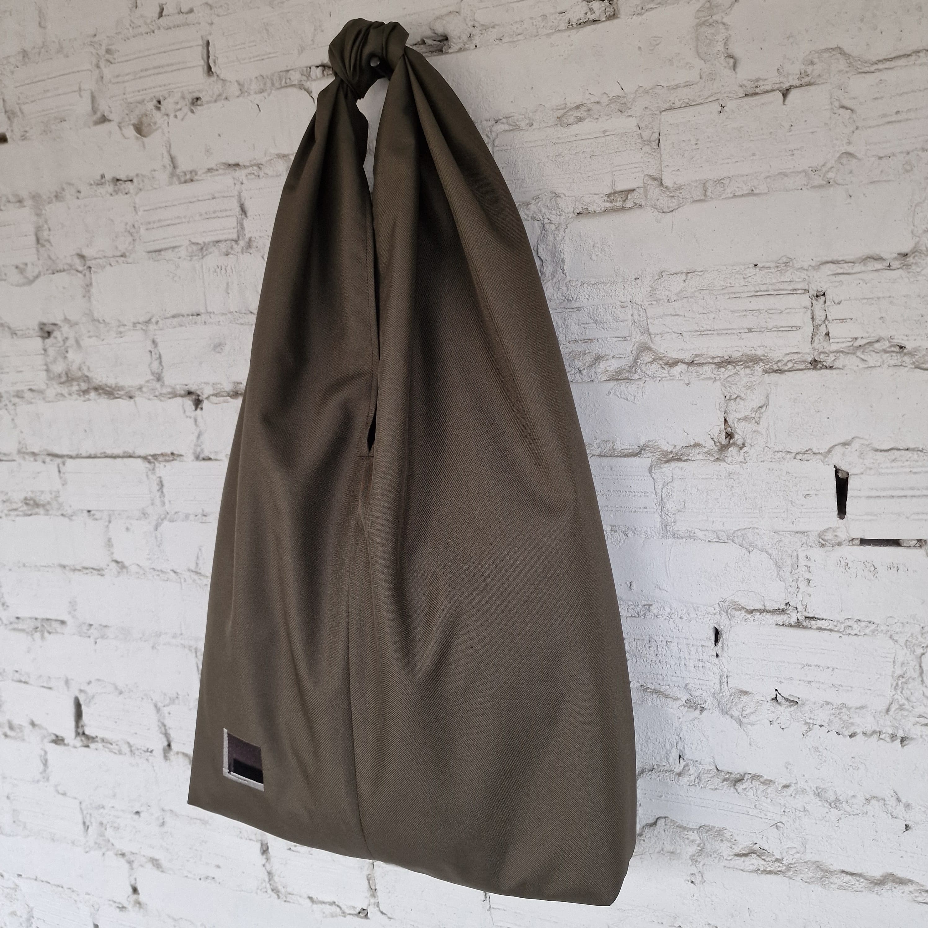 Khaki drawstring bag hanging against a white brick wall