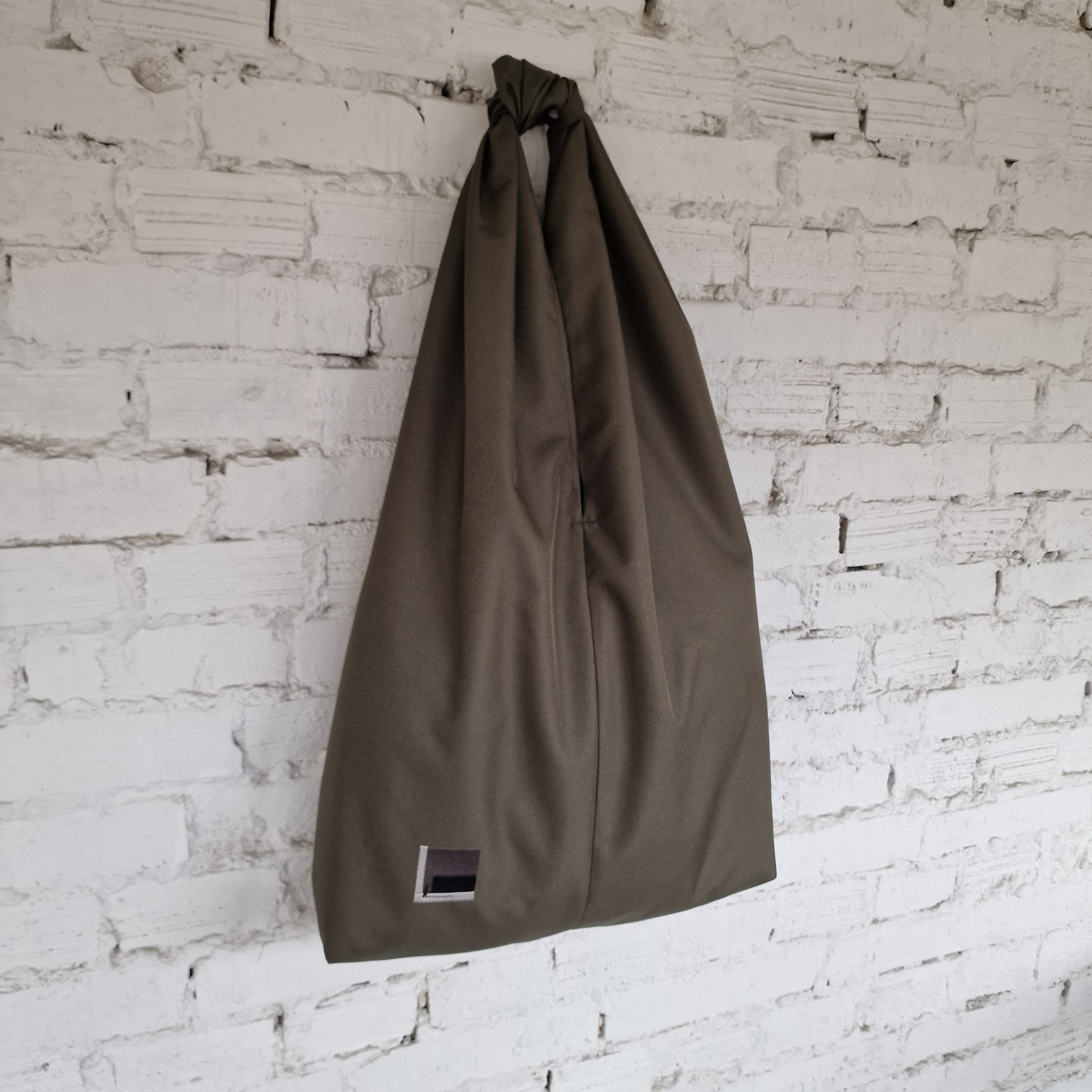 Khaki HOBO bag hanging against a white brick wall