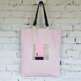 Pink tote bag with a small rectangular design on a white brick wall background