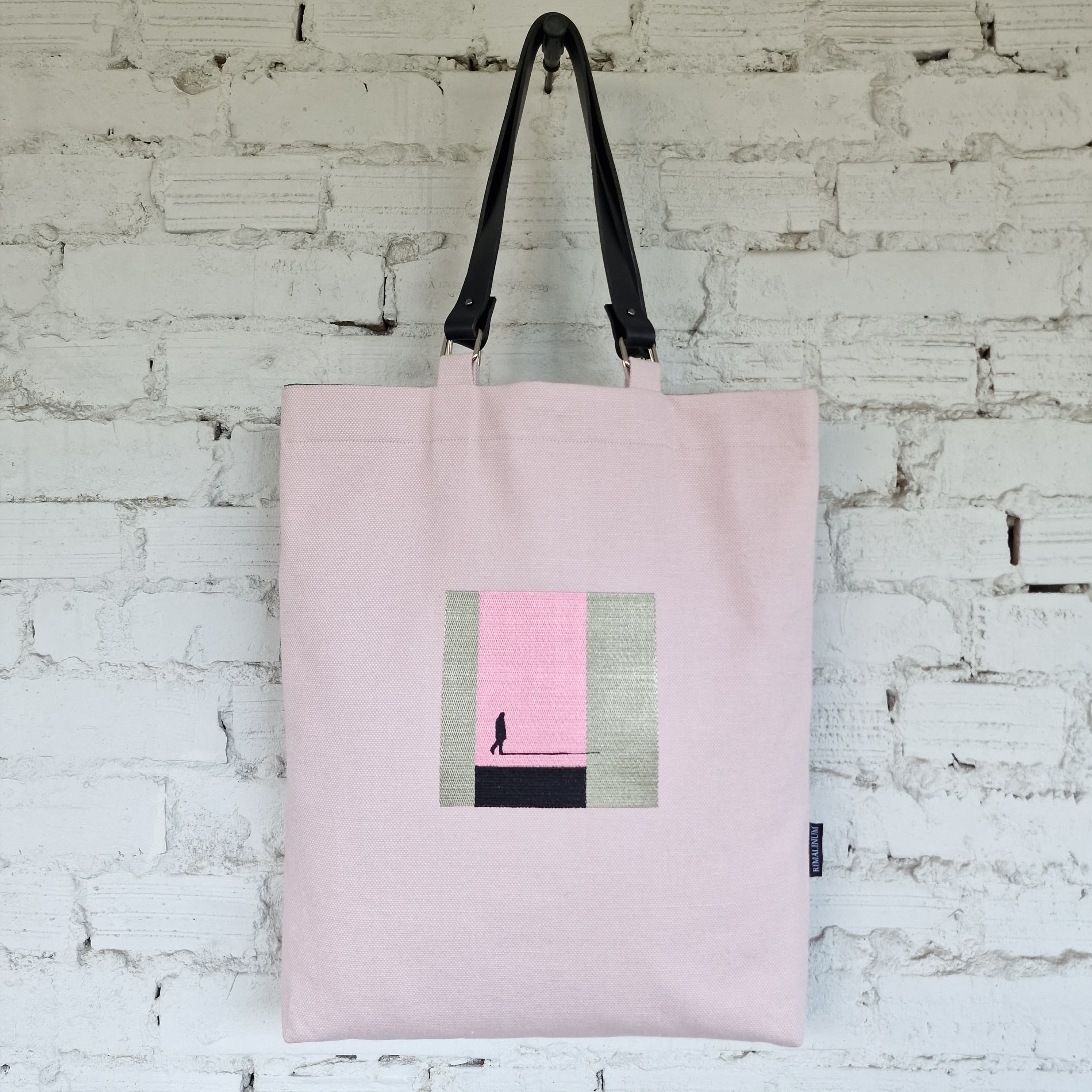 Pink tote bag with a small rectangular design on a white brick wall background
