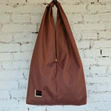 Rust brown waterproof hobo bag handmade from impregnated fabric, minimalist design on a white brick background