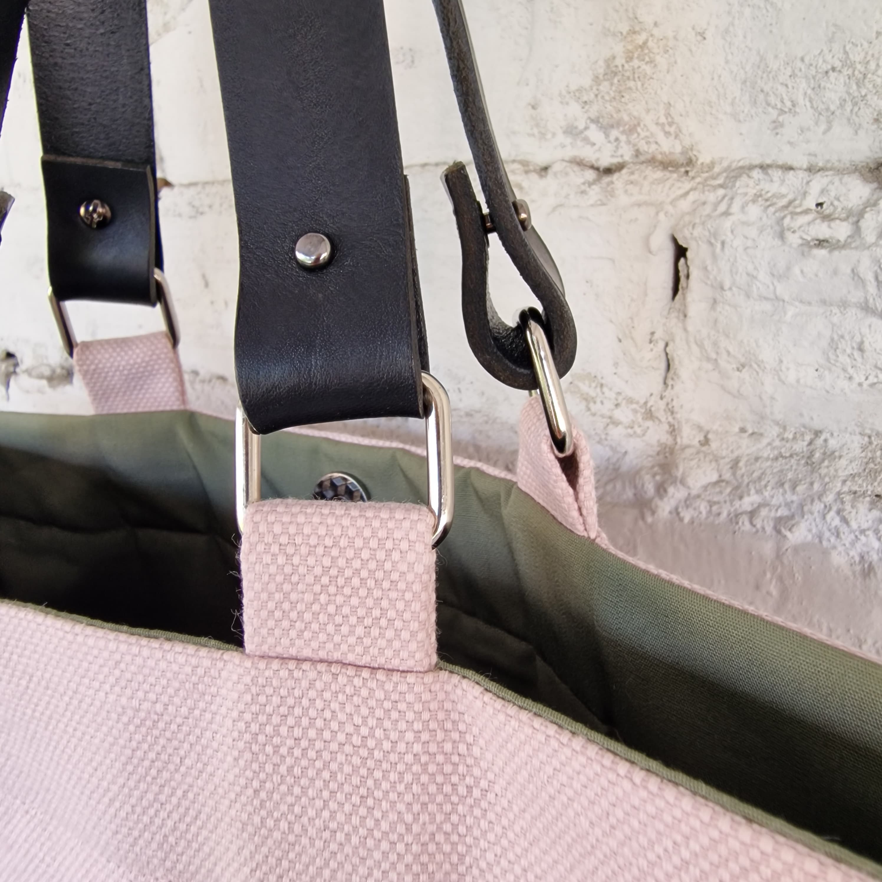 Close-up of a bag with a black strap and pink padding against a textured wall.