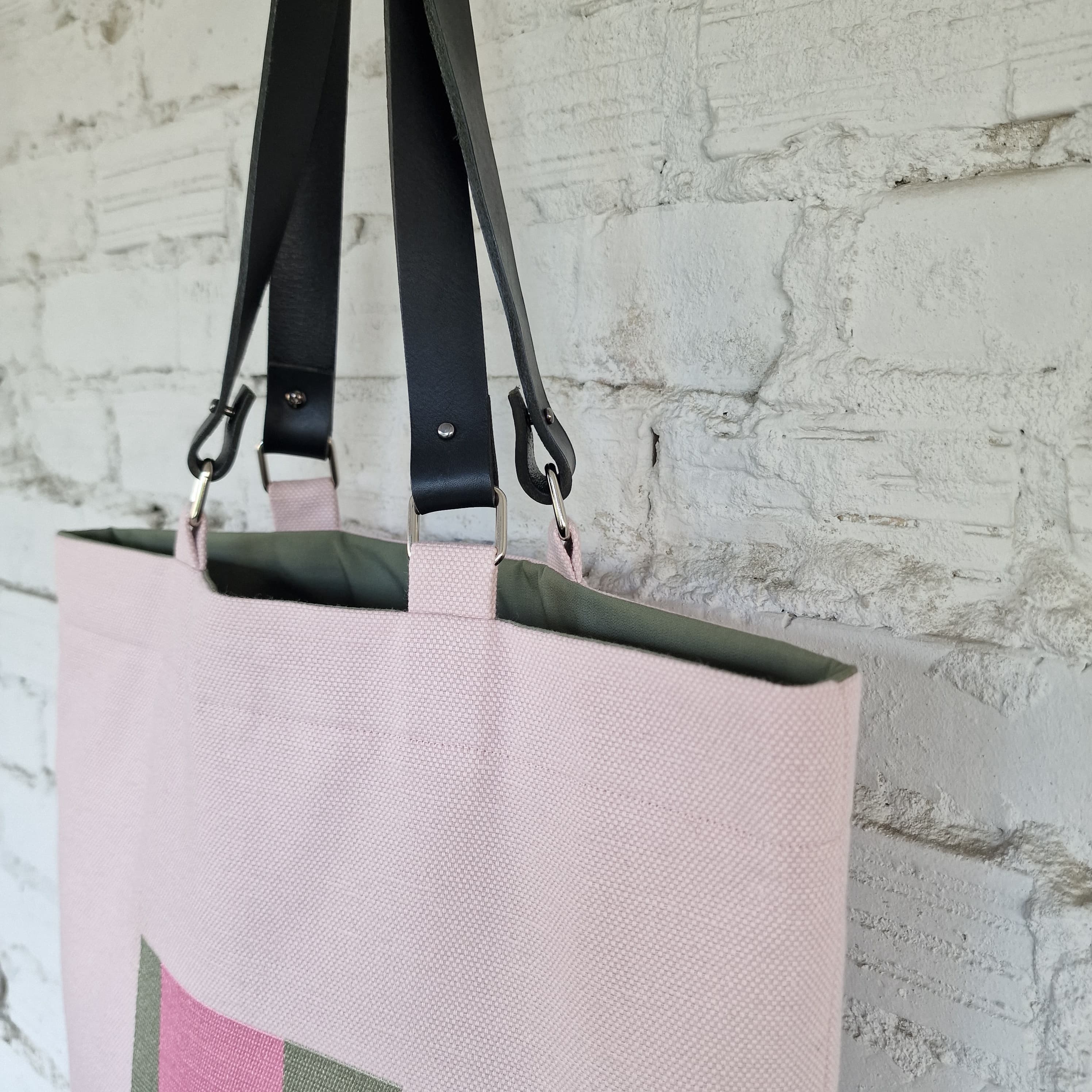 Pink tote bag with black straps against a textured white brick wall.