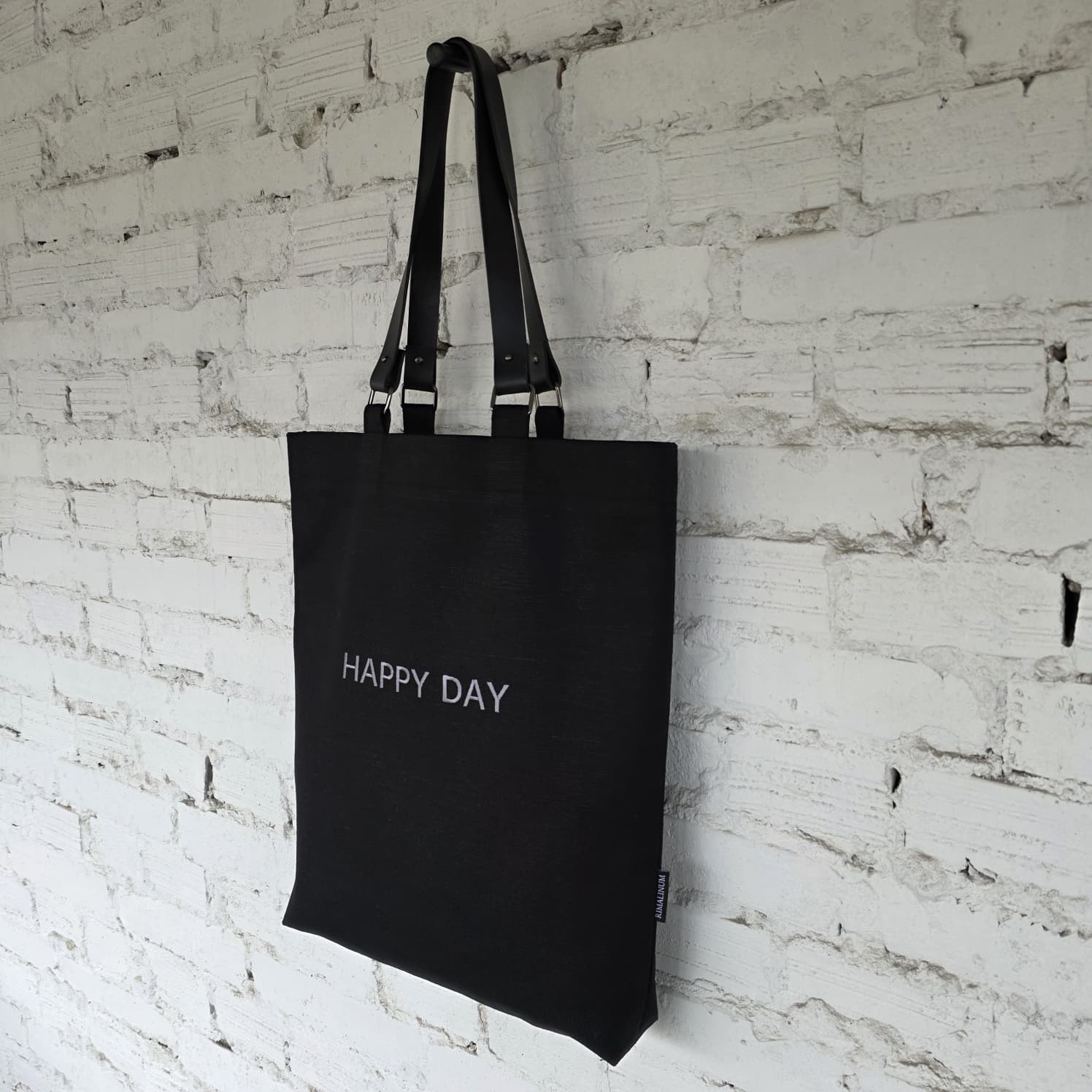 Close-up of removable genuine leather handles with metal hardware on a black linen-cotton tote bag, showing stitching and craftsmanship