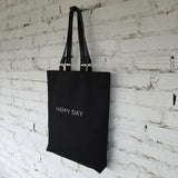 Close-up of removable genuine leather handles with metal hardware on a black linen-cotton tote bag, showing stitching and craftsmanship