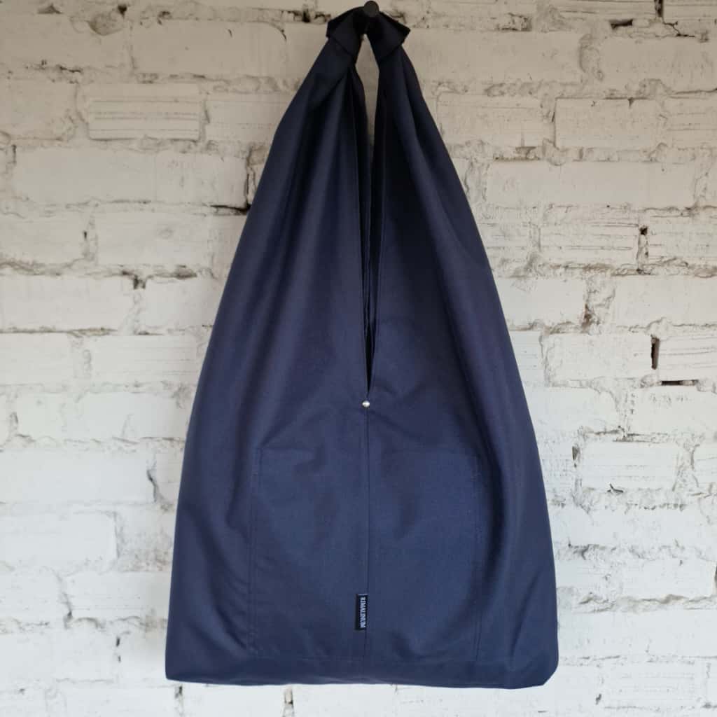 Navy blue drawstring bag hanging against a white brick wall