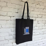 Black linen tote bag with blue geometric embroidery and leather handles
