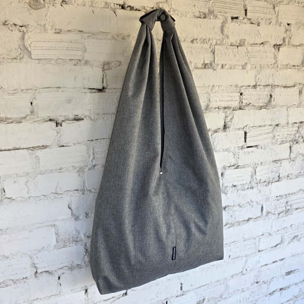 Gray tote bag hanging against a white brick wall
