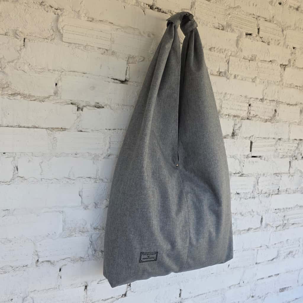 Gray tote bag hanging against a white brick wall