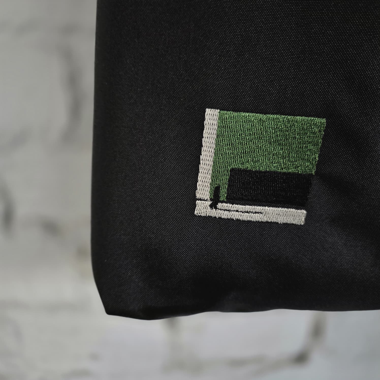 Detailed embroidery of The Path Finder bag — olive green thread on black textile.