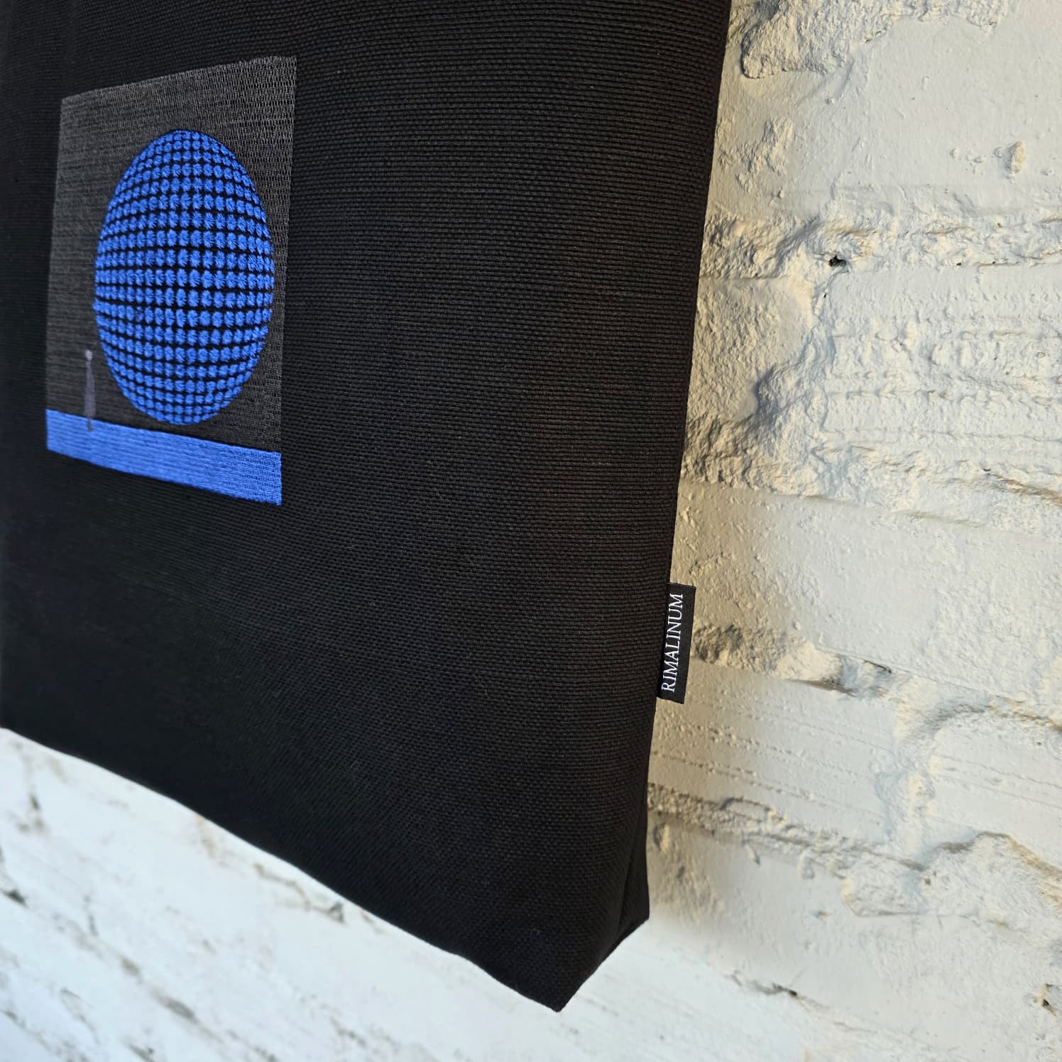 Blue circular 3D embroidered design on black tote bag, modern geometric textile art detail